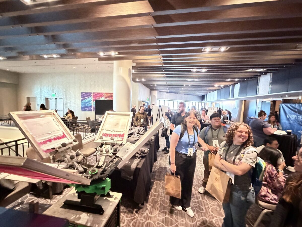 Guests holding kraft merch bags beside a live screen-print station at a conference