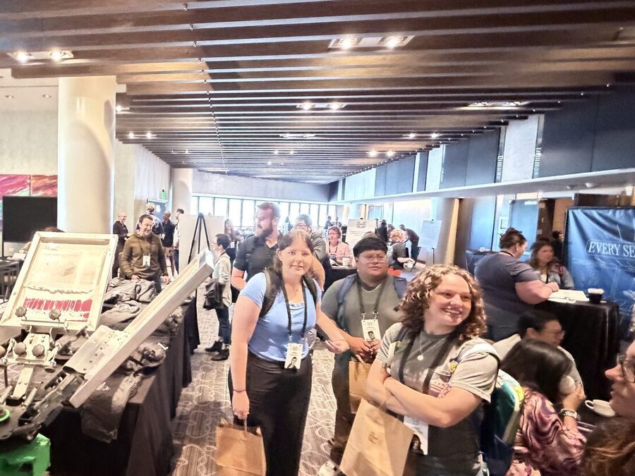 Smiling conference guests holding kraft merch bags beside a live press