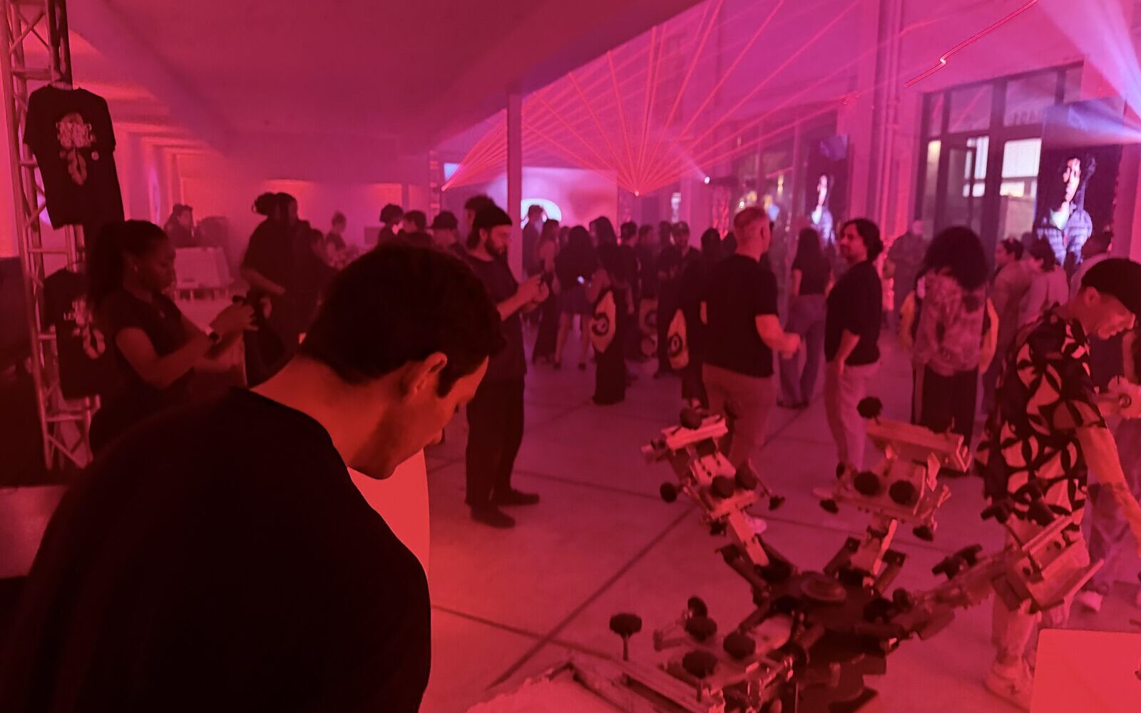 A nighttime crowd under magenta laser lighting beside a live print carousel