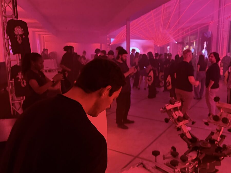 A printed tee hanging on a truss beside a live press carousel under magenta laser lighting