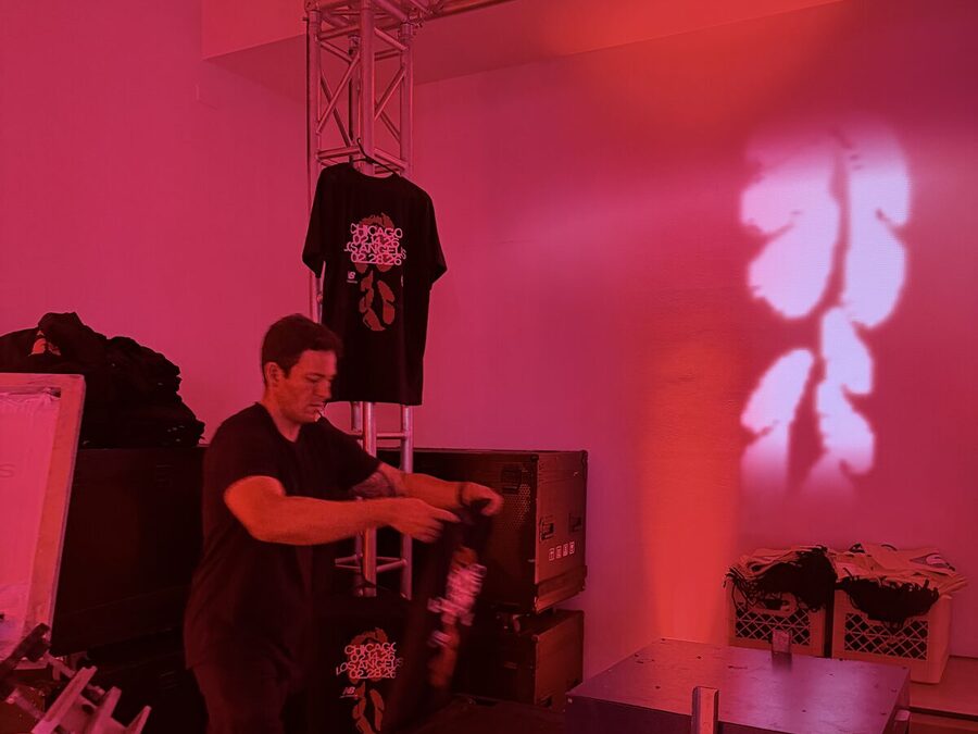 A freshly printed black tee on a truss under magenta stage lighting at a live print station