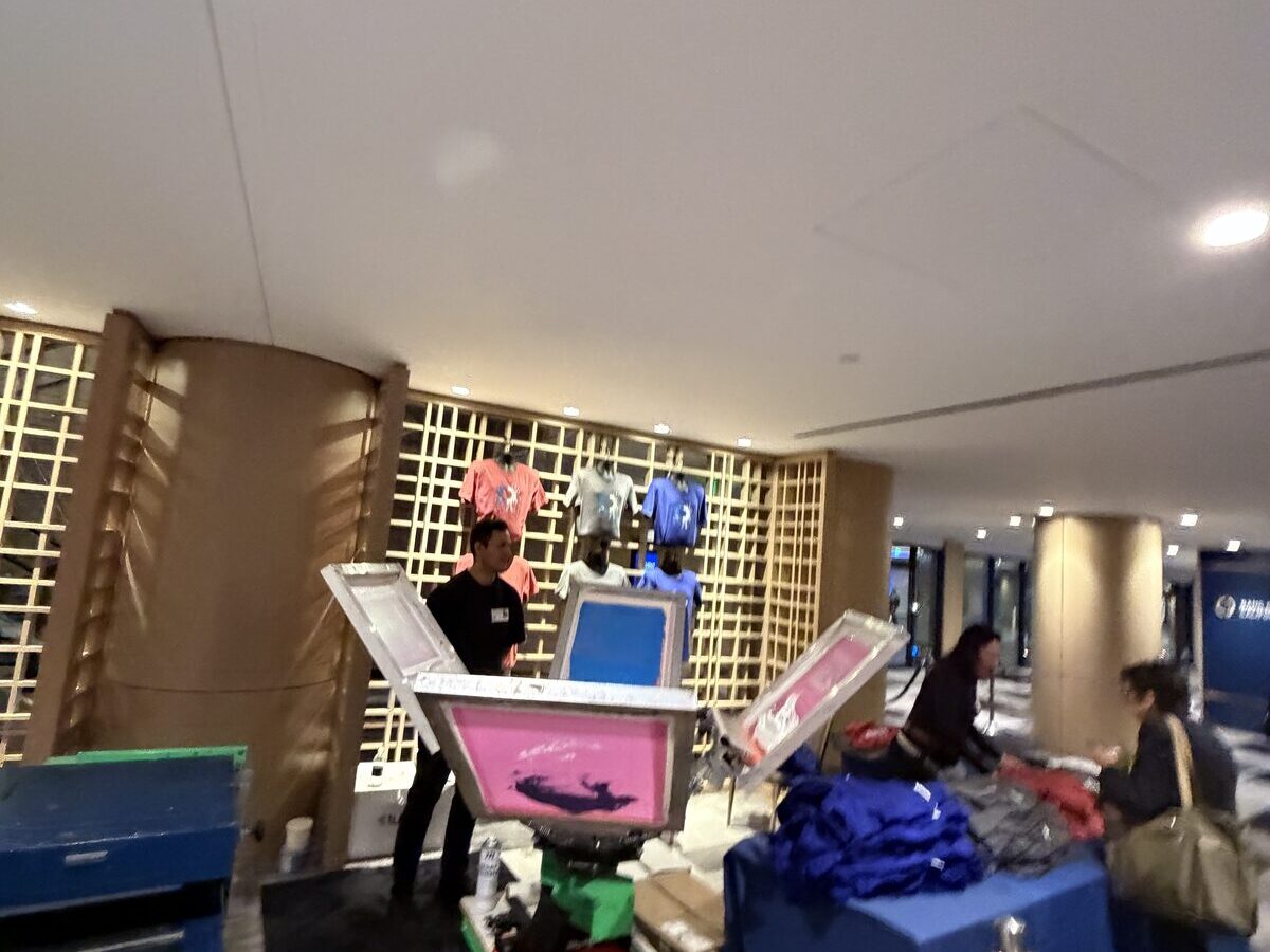 A live screen-print station with pink and blue screens and finished tees at an activation